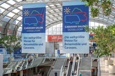 Photo for Duesseldorf Germany 01.09.2019 Banners hang under a glass roof saying in german the worlds largest fair for motorhomes and caravans. Visitors walking in and using escalators - Royalty Free Image