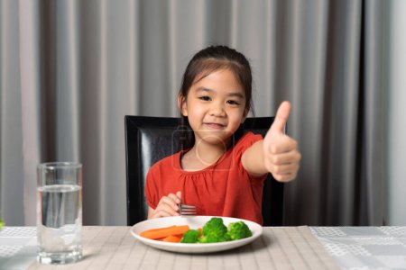 Téléchargez les photos : Petite fille mignonne montrant pouce montrant manger des légumes sains. - en image libre de droit