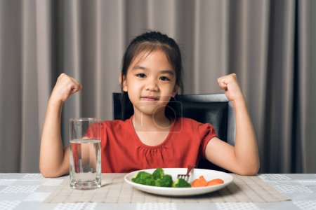 Téléchargez les photos : Enfant montre la force de manger des légumes et des aliments nutritifs. - en image libre de droit
