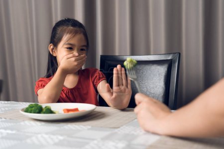 Téléchargez les photos : Petite fille mignonne refusant de manger des légumes sains. Les enfants n'aiment pas manger des légumes. - en image libre de droit