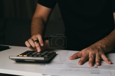 Téléchargez les photos : Asiatique homme utilise une calculatrice pour calculer ses dépenses mensuelles diverses à la maison. - en image libre de droit