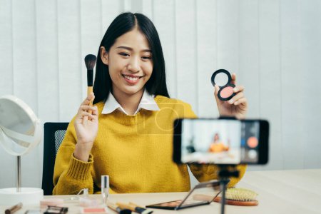 Téléchargez les photos : Jeune blogueur beauté asiatique présente des produits cosmétiques ainsi que des tutoriels sur la façon d'appliquer et d'enregistrer des tutoriels de maquillage sur les réseaux sociaux. - en image libre de droit
