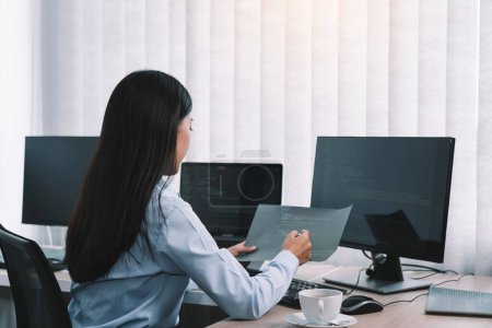 Téléchargez les photos : Asiatique femme développeurs de logiciels assis devant les ordinateurs en regardant les codes informatiques sur l'écran. - en image libre de droit