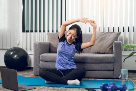 Téléchargez les photos : Asiatique femme étirement pendant un cours de yoga avec un entraîneur à son ordinateur portable à la maison. - en image libre de droit