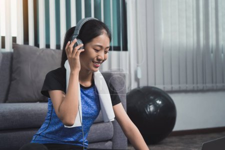 Téléchargez les photos : Asiatique belle jeune femme en utilisant ordinateur portable et écouteurs écouter de la musique tout en pratiquant l'exercice yoga à la maison. - en image libre de droit