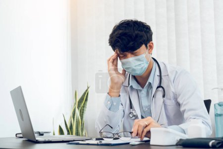 Téléchargez les photos : Asiatique jeune homme médecin être épuisé et burnout dans la salle de bureau. - en image libre de droit