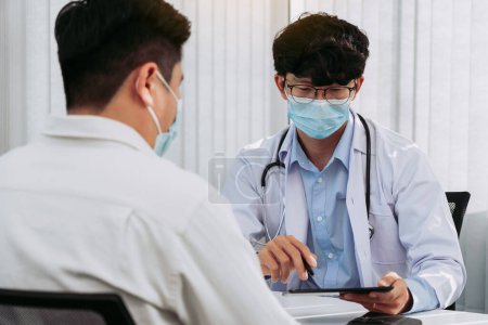 Téléchargez les photos : Les médecins expliquent le traitement d'un patient malade dans des comprimés tout en portant un masque pendant l'épidémie de virus. - en image libre de droit
