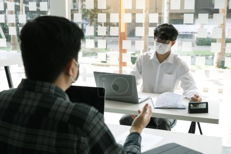 Téléchargez les photos : Un collègue asiatique travaille en portant un masque au bureau pendant la COVID-19. - en image libre de droit