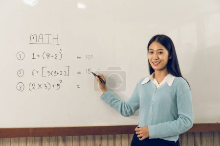 Téléchargez les photos : Asiatique enseignante enseigne étudiants à la salle de classe tout en pointant vers les chiffres sur le tableau blanc. - en image libre de droit