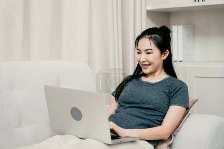 Téléchargez les photos : Asiatique femme se repose sur le canapé en utilisant un ordinateur portable pour travailler à la maison. - en image libre de droit