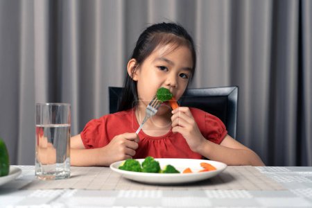 Téléchargez les photos : Asiatique petite fille manger des légumes sains avec plaisir. - en image libre de droit