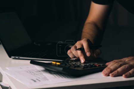 Téléchargez les photos : Asiatique homme utilise une calculatrice pour calculer les frais divers mensuels de sa famille à sa maison. - en image libre de droit