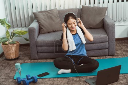 Téléchargez les photos : Asiatique belle jeune femme en utilisant ordinateur portable et écouteurs écouter de la musique tout en pratiquant l'exercice yoga à la maison. - en image libre de droit