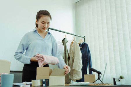 Téléchargez les photos : Entrepreneur asiatique prépare ses vêtements qui peuvent être vendus dans des boîtes en papier pour la livraison aux clients. - en image libre de droit