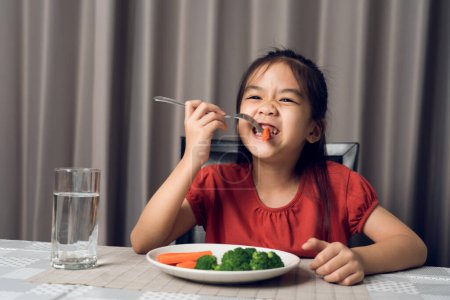 Téléchargez les photos : Asiatique petite fille manger des légumes sains avec plaisir. - en image libre de droit