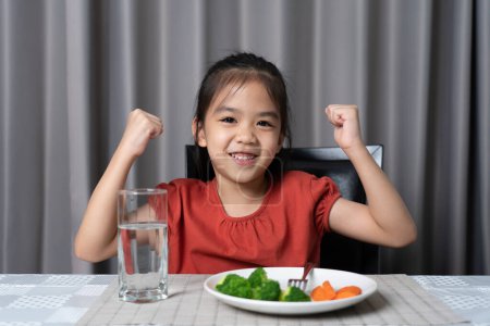 Téléchargez les photos : Enfant montre la force de manger des légumes et des aliments nutritifs. - en image libre de droit