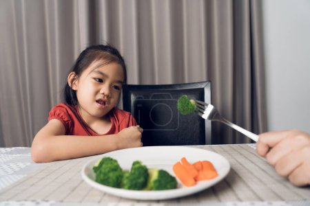 Téléchargez les photos : Petite fille mignonne refusant de manger des légumes sains. Les enfants n'aiment pas manger des légumes. - en image libre de droit