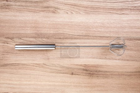 Stainless manual egg beating tool on a wooden cutting board