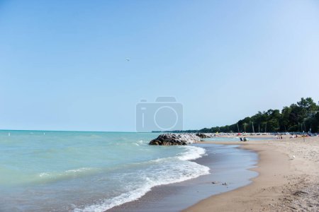 Chicago, IL, USA - 27. August 2023: Strand in der Nähe des Michigansees. Raue Wellen. Ein Haufen großer Steine in der Nähe des Sees und des Strandes. Die Leute entspannen sich am Strand.