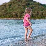 Little girl playing on the sea sandy beach. A girl in a pink t-shirt and swimming trunks on a beautiful sea beach. Cleanest tranquise water of Adriatic sea.
