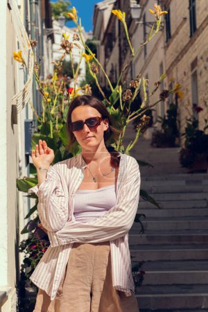 A young girl in sunglasses travels through Europe and poses against the background of a long staircase and potted plants growing on the staircase street. The girl enjoys freedom and travel. Girl tourist in an Italian city.