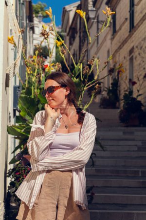 A young girl in sunglasses travels through Europe and poses against the background of a long staircase and potted plants growing on the staircase street. The girl enjoys freedom and travel. Girl tourist in an Italian city.