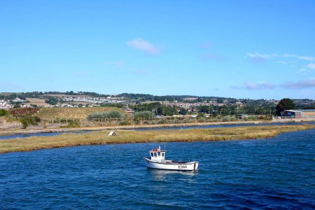 Foto de AXMOUTH, Reino Unido - 30 de agosto de 2022 - Pequeño barco pesquero amarrado a lo largo del río Axe con el campo de Devon en la parte trasera, Axmouth, Devon, Reino Unido, Europa, 30 de agosto de 2022. - Imagen libre de derechos