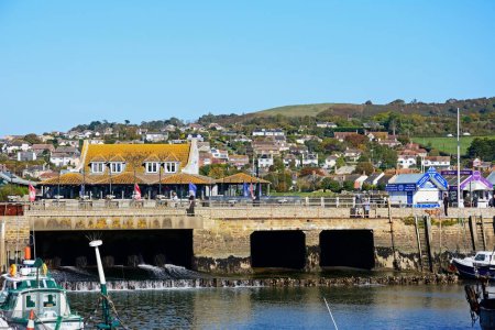 Foto de WEST BAY, Reino Unido - 10 de octubre de 2022 - Barcos pesqueros tradicionales amarrados en el puerto en marea baja con vistas hacia la compuerta y los edificios de la ciudad, West Bay, Dorset, Reino Unido, Europa, 10 de octubre de 2022. - Imagen libre de derechos