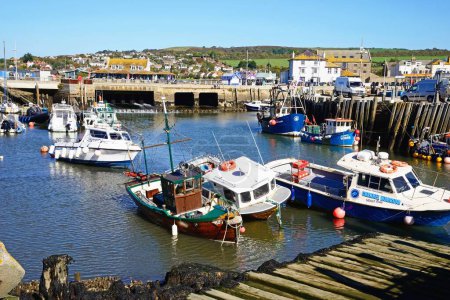 Foto de WEST BAY, Reino Unido - 10 de octubre de 2022 - Vista de los barcos de pesca tradicionales amarrados en el puerto en marea baja con la ciudad y el campo en la parte trasera, West Bay, Dorset, Reino Unido, Europa, 10 de octubre de 2022. - Imagen libre de derechos