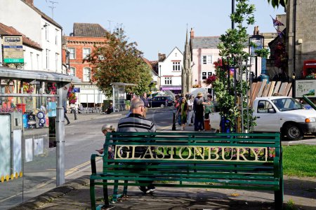 Téléchargez les photos : GLASTONBURY, Royaume-Uni - 05 septembre 2023- Homme assis sur un banc de fer le long de la rue Magdalene avec des magasins du centre-ville à l'arrière, Glastonbury, Somerset, Royaume-Uni, Europe, 05 septembre 2023. - en image libre de droit