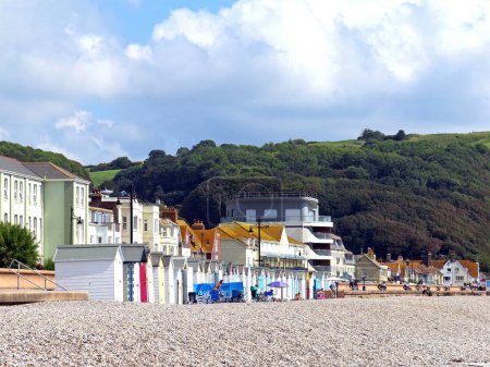 Foto de SEATON, Reino Unido - 02 de septiembre de 2023 - Turistas y cabañas de playa a lo largo de la playa con edificios urbanos en la parte trasera, Seaton, Devon, Reino Unido, Europa, 02 de septiembre de 2023. - Imagen libre de derechos
