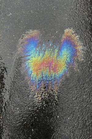 Farbbild von auslaufendem Heizöl auf Asphalt. Regenbogenfarben von Ölresten auf Wasser.