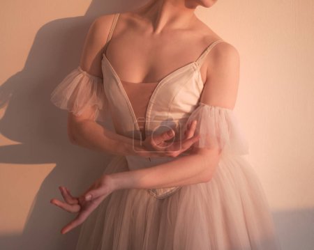 A beautiful ballerina poses in a studio in a beautiful dress with a decollete. Hands perform ballet movements. photo shows the beauty of classical ballet.
