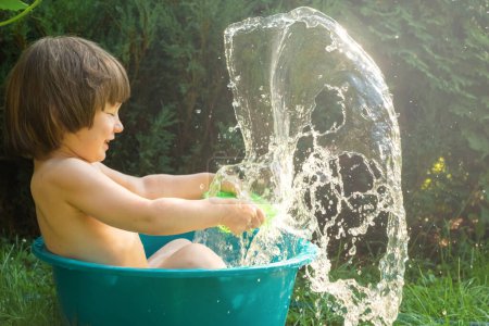 Photo for Baby is splashing in a bowl of water. Big splashes. Summer concept, sunny day - Royalty Free Image
