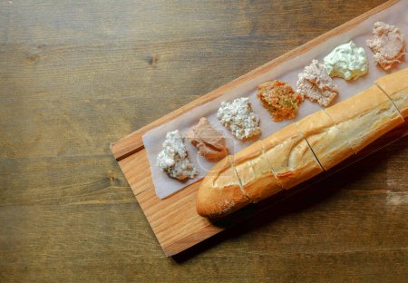 Verschiedene Brotaufstriche und frisches französisches Baguette auf einem Holztisch. Herzhaftes Frühstück. Verschwommener und selektiver Fokus