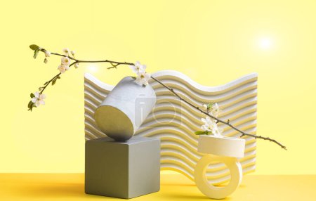Yellow gradient background with geometric texture shapes. Cubic white and gray podiums and cherry blossom branches. Still life. Spring concept.