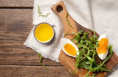Nahaufnahme von Rucola, gekochtem Ei und Olivenöl auf einem Holzbrett. Gesundes vegetarisches Frühstück. Blick von oben 
