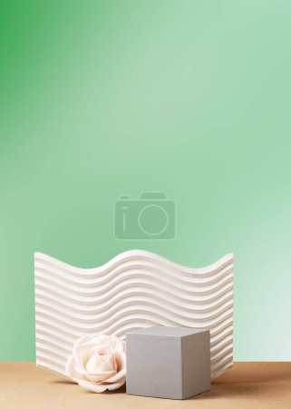 Green gradient background with geometric texture shapes. Cubic gray podium and cream rose. Still life.