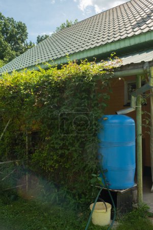 Téléchargez les photos : Réservoir de collecte d'eau sous un toit avec un drain. Architecture de récolte de l'eau de pluie. Photo verticale. Journée ensoleillée - en image libre de droit