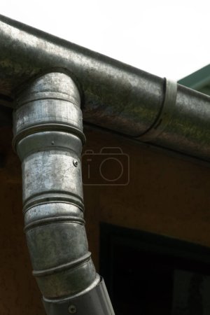 Téléchargez les photos : Gouttière d'eau de pluie sous le toit de la maison. Architecture de récolte de l'eau de pluie. Concentration floue et sélective. Photo verticalePhoto verticale - en image libre de droit