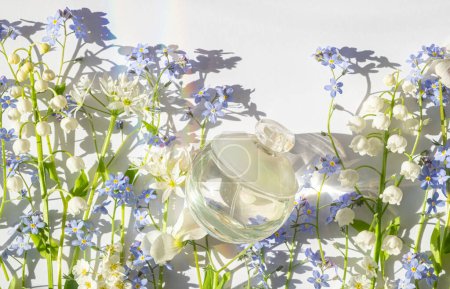 Cosmetic glass transparent bottle and spring flowers lilies of the valley and glare from the sun on a white background. Blur and selective focus 