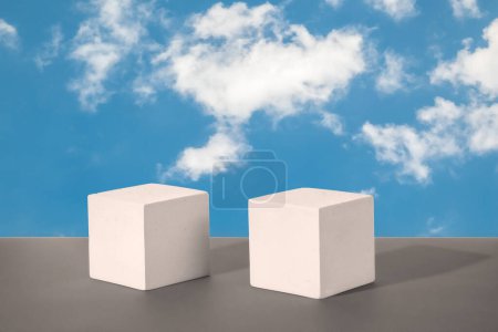 Two cement cubic podiums on a blue sky with white clouds. Mockup for the demonstration of cosmetic products. Copy space