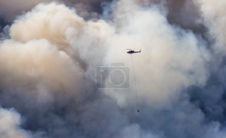 Téléchargez les photos : Wildfire Service Helicopter survolant BC Forest Fire and Smoke sur la montagne près de Hope par une chaude journée d'été ensoleillée. Colombie-Britannique, Canada. Catastrophe naturelle - en image libre de droit