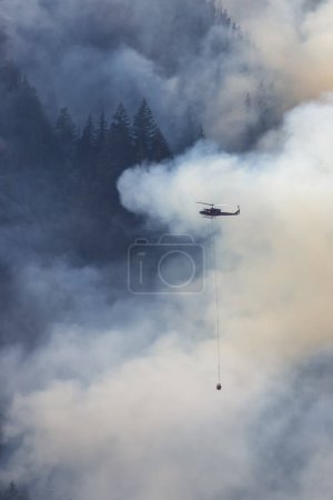 Photo for Wildfire Service Helicopter flying over BC Forest Fire and Smoke on the mountain near Hope during a hot sunny summer day. British Columbia, Canada. Natural Disaster - Royalty Free Image