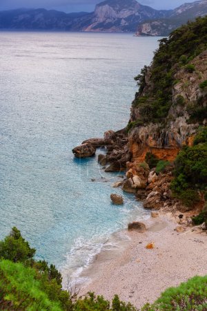 Téléchargez les photos : Sandy Beach on a rocky coast near Cala Gonone, Sardinia. Cloudy Sunrise Sky. - en image libre de droit