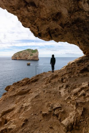 Foto de Adventurous Woman in a Cave on Rocky Coast with Cliffs on the Mediterranean Sea. Regional Natural Park of Porto Conte, Sardinia, Italy. Adventure Travel - Imagen libre de derechos