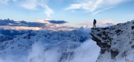 Téléchargez les photos : Adventurous Man Hiker standing on top of icy peak with rocky mountains in background. Adventure Composite. 3d Rendering rocks. Aerial Image of landscape from BC, Canada. Dramatic Sky - en image libre de droit