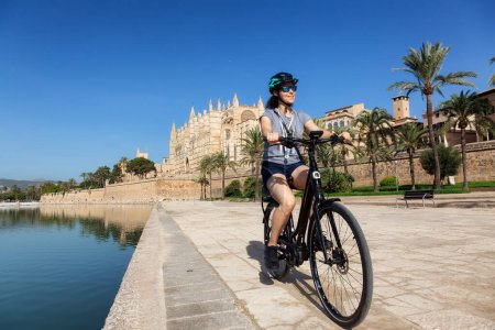 Téléchargez les photos : Adventure Travel Femme en vélo près de Catedral-Basilica de Santa Maria de Mallorca à Palma, Îles Baléares, Espagne. Journée ensoleillée. - en image libre de droit