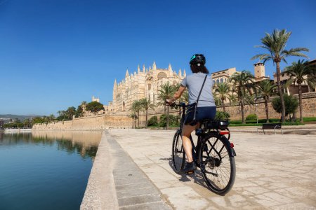 Téléchargez les photos : Adventure Travel Woman on a Bicycle riding near Catedral-Basilica de Santa Maria de Mallorca in Palma, Balearic Islands, Spain. Sunny Day. - en image libre de droit