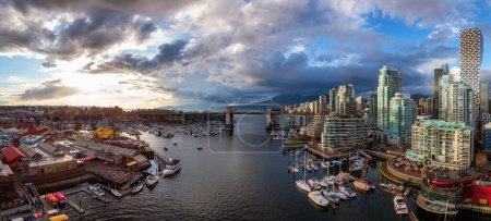 Téléchargez les photos : Vue aérienne panoramique de l'île Granville à False Creek avec des toits modernes de la ville et des montagnes en arrière-plan. Centre-ville de Vancouver, Colombie-Britannique, Canada. Coucher de soleil - en image libre de droit